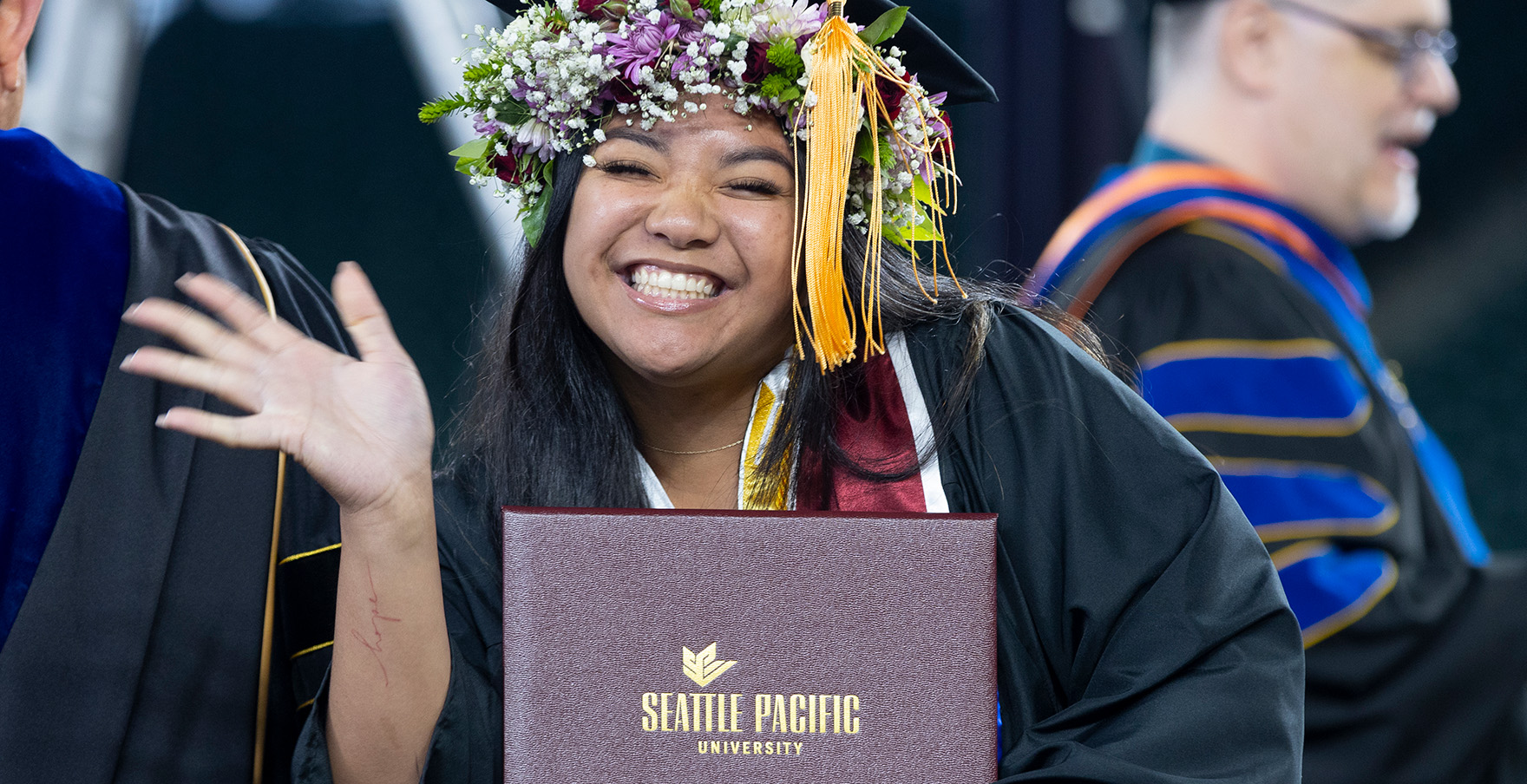 An SPU student smiles and waves with her diploma | photo by Mike Siegel