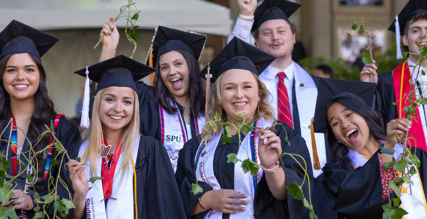 Excited students in their caps and gowns proudly hold up their ivy at SPU