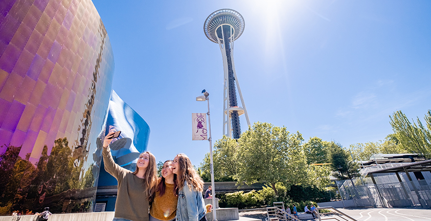 Three female students taking a selfie in front of the Seattle Space Needle
